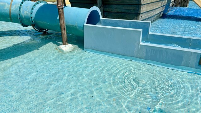 Closeup of a children's water slide in a shallow splash pool at an outdoor water park with clear blue water on a sunny summer day