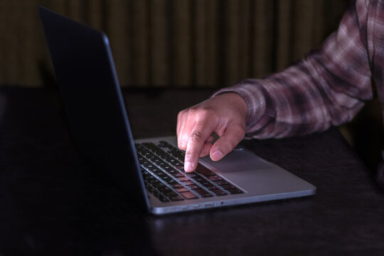 Close-up of hand pressing key on laptop keyboard illuminated in the dark