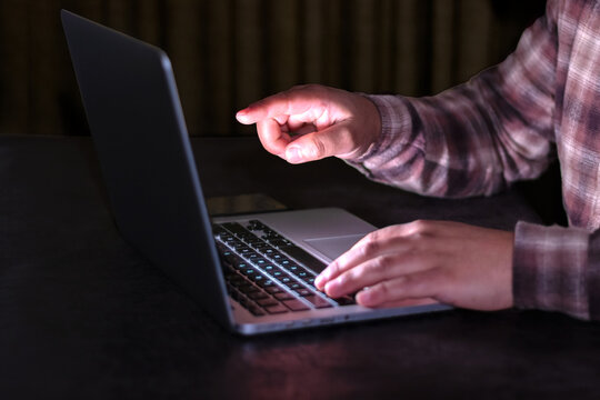 Side view of hands using laptop in the dark with index finger pointing at the screen
