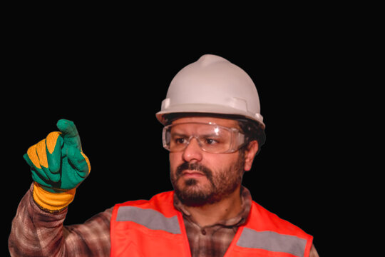 Industrial engineer in hard hat, goggles, and gloves directing at touch screen or futuristic interface on black background