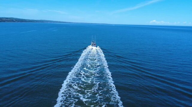 A fishing boat moves across the wide St. Lawrence River, its wake stretching behind in the still water.