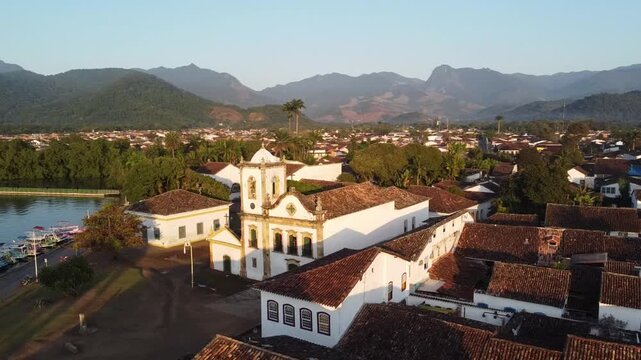 Drone orbit of Paraty church at sunrise with mountains and bay in background, Brazil