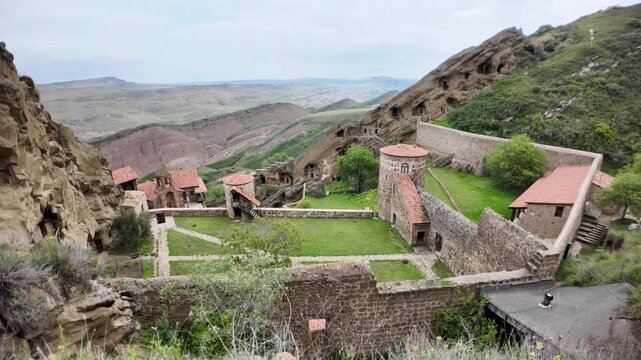 David Gareji monastery, a historic rock-hewn orthodox complex in Georgia, featuring multiple carved caves, ancient stone walls, and a green courtyard under a cloudy sky