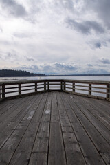Obraz premium Wooden pier balcony extending toward calm water under dramatic skies in Vancouver, British Columbia