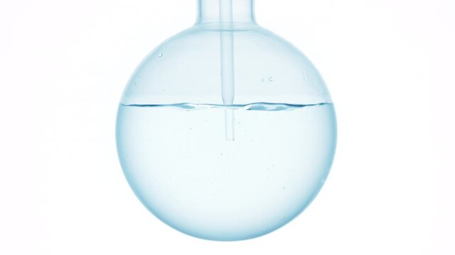 Closeup of pale blue liquid injected through a long dropper into a round-bottom flask, causing swirls and bubbles against a white surface | Ethoxydiglycol solution cosmetic product ingredient concept