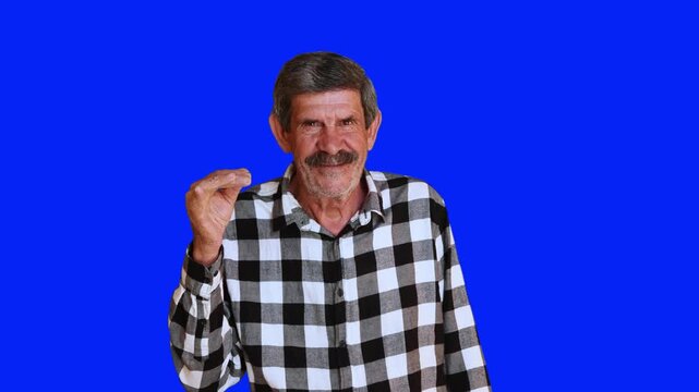 Smiling senior man making a money gesture with fingers on blue chroma key background. Positive elderly person looking at camera. 4K video.