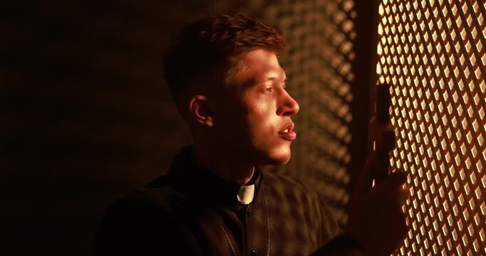 Priest with cross talking to parishioner near wooden window in confessional booth