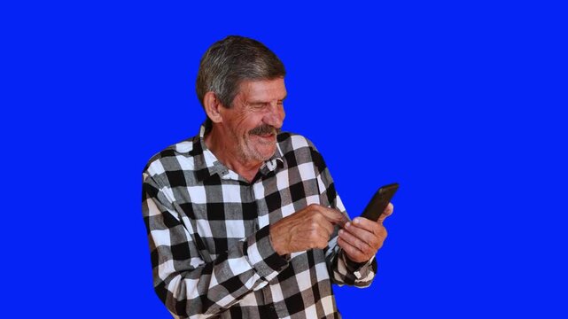 Smiling senior man using a smartphone on blue chroma key background. Happy elderly person interacting with a mobile phone. 4K video.