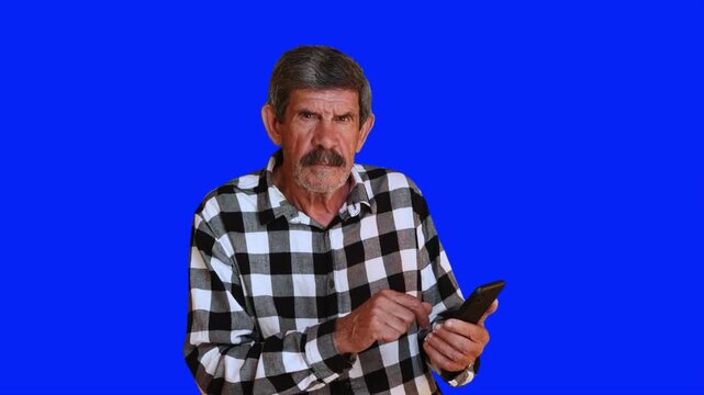 Serious senior man using a smartphone on blue chroma key background. Elderly person looking concerned while interacting with a mobile phone. 4K video.