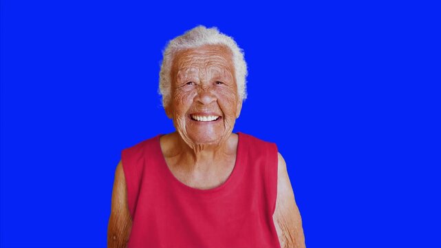 Happy senior woman laughing on blue chroma key background. Joyful elderly female looking at camera with genuine smile and positive expression. 4K video.