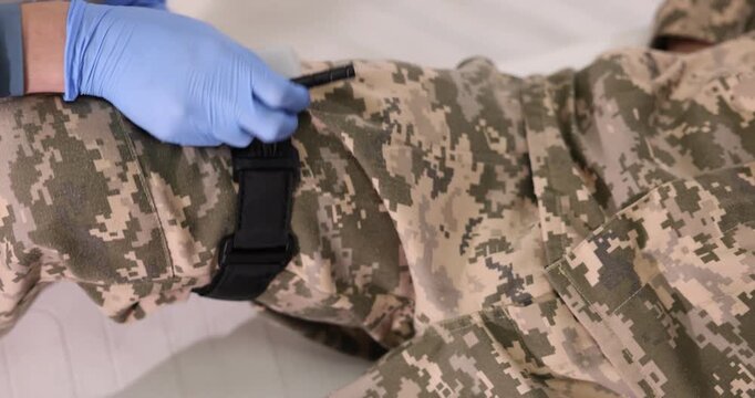 Doctor applying tourniquet on soldier's leg indoors, closeup