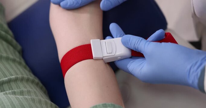 Doctor applying medical tourniquet on patient's arm indoors, closeup