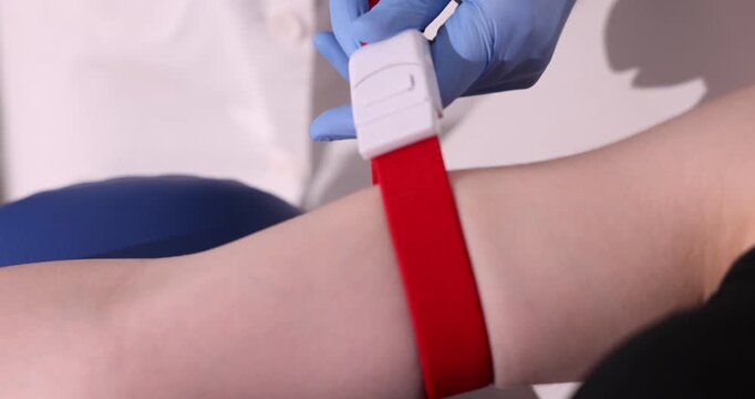 Doctor applying medical tourniquet on patient's arm indoors, closeup
