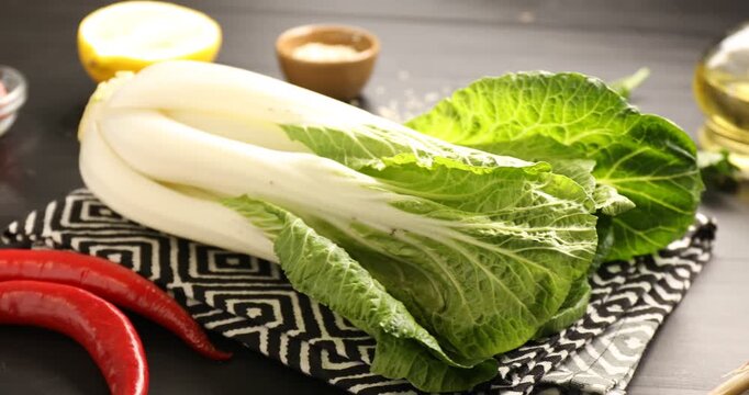 Fresh bok choy cabbage and other products on black wooden table, closeup. Camera moving left