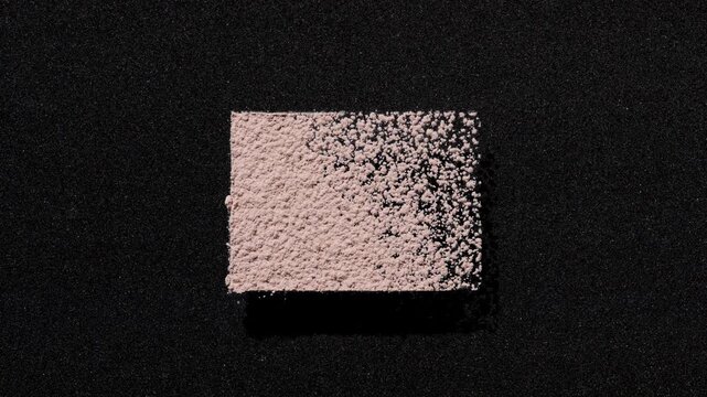 Overhead capture of beige powder sifted into a rectangle on a black background | Concept for powder foundation product campaign