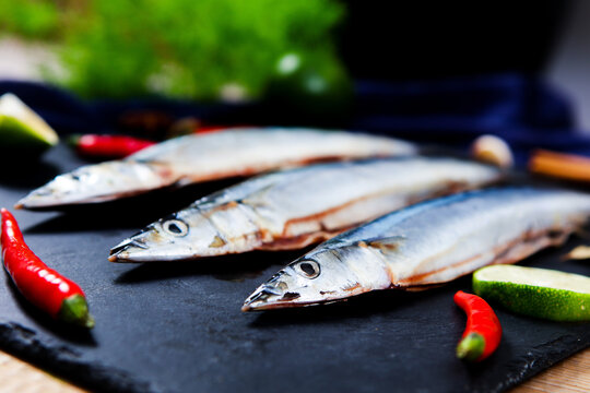 Raw saury fish surrounded by chili garlic lime star anise dark slate