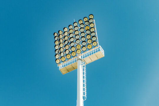 Large stadium floodlight tower rises against a clear deep blue sky.
