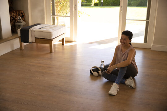 Asian woman sitting on wood floor by doors in sneakers, water bottle, headphones, copy space