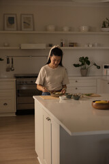 Asian woman preparing meal at residential kitchen island, chopping on board and stirring bowl © wavebreak3
