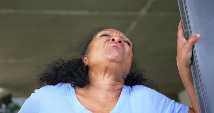 Senior African American woman in blue shirt at doorframe gripping right-hand tilting back grimacing