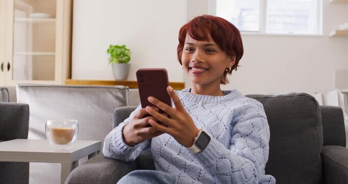 African American woman 20s in blue sweater on sofa smiling, holding red phone, responding to noise