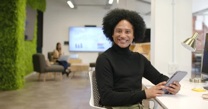 Coworkers in office lounge, male 30s tapping tablet and looking up, smiling and engaging camera