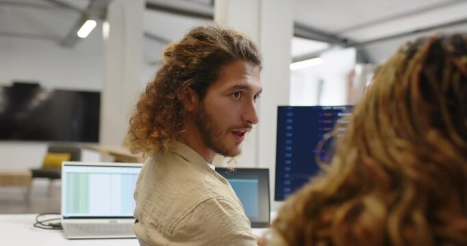 Diverse coworkers watching male dev reviewing code and checking monitors and laptop at office desk