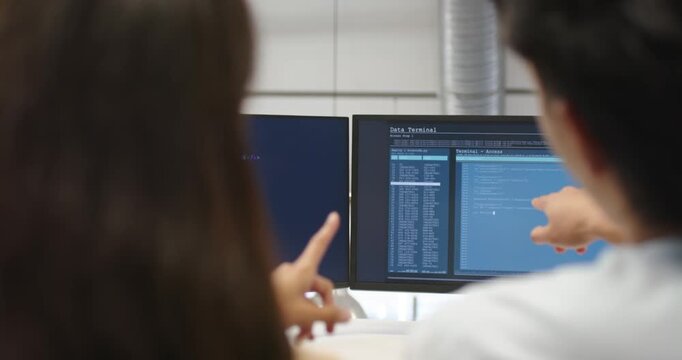 Diverse coworkers analyzing security code on monitors at desk right pointing causing left gesturing