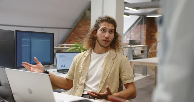 Adult man listening and responding to standing coworker in loft office, pointing at laptop charts