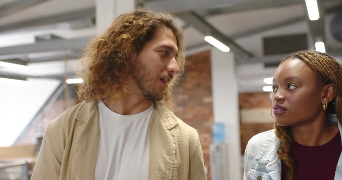 Diverse coworkers walking in office, man turning and discussing work, woman reacting by brick wall
