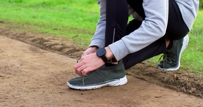 Adult man picking up loose shoelace, tying green running shoe on dirt path, preparing for run