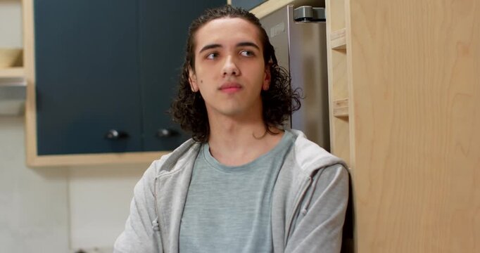 African American man leaning against fridge, shifting gaze, listening to off frame voice in kitchen