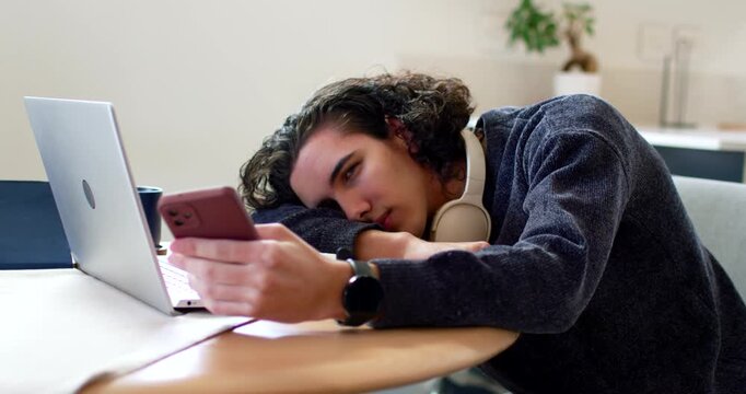 African American man feeling tired, scrolling phone, placing phone by laptop and dozing in study