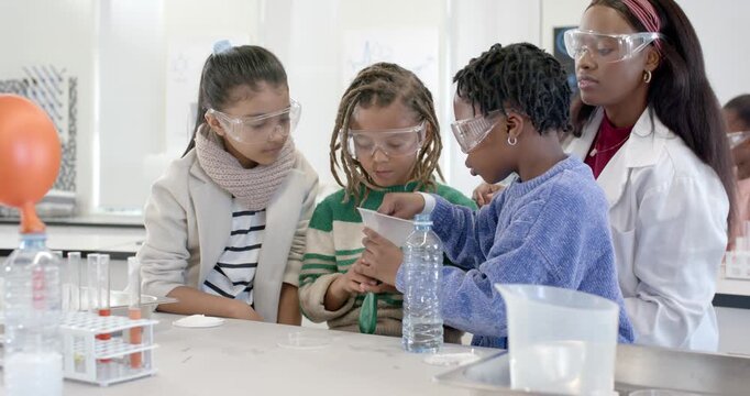 Diverse children after teacher cue conducting funnel demo at lab bench, stirring to inflate balloon