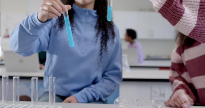 Two African youth females spotting filled test tubes in rack, lifting tubes, comparing blue liquid