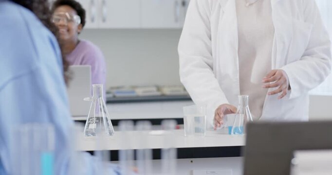 Indian female student reaching for blue cup after placement on lab bench, demonstrating with flask