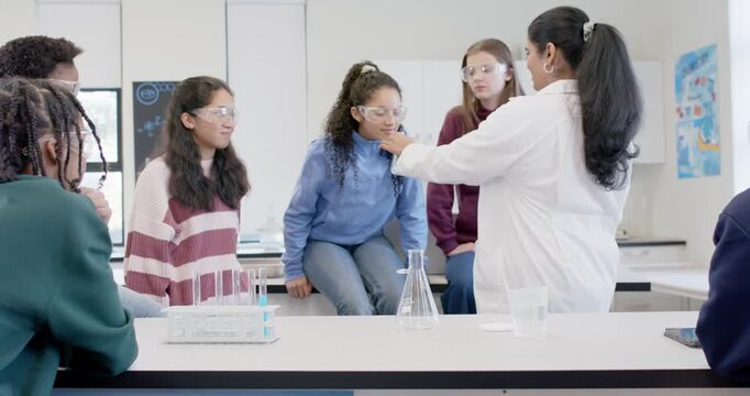 Female Indian instructor with youth girls starting demo holding flask at lab bench, allowing view