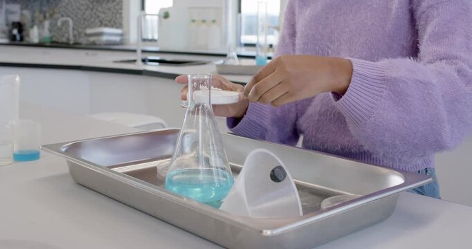 African youth female placing dish over Erlenmeyer at bench, scraping sample into flask, copy space