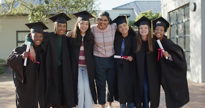 Diverse graduates linking arms, fixing caps on campus as camera pulling back, posing for portrait