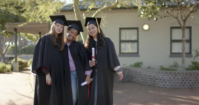 African American female graduates posing after graduation holding diplomas, wearing gowns on campus