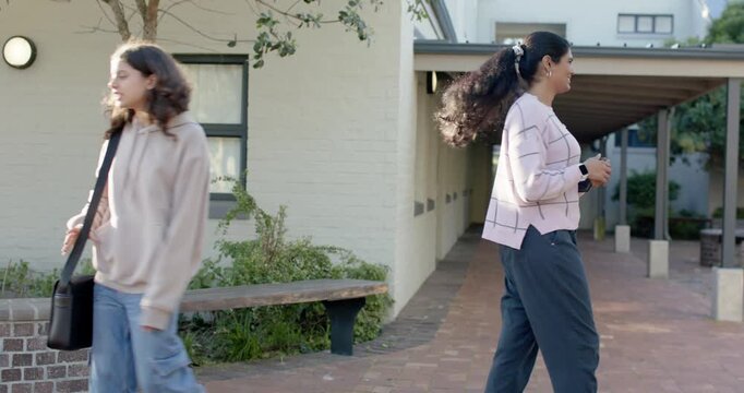 Diverse women greeting, right student raising hand with tablet, passing to class on brick path