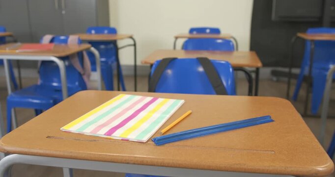 Camera is shifting and refocusing near classroom desk to highlight pastel notebook, pencil, case