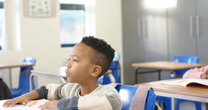 African American child in sweater after teacher asks raising hand, speaking in class with pencil