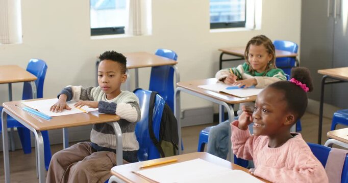 African kids sitting at desks by windows as teacher asking question, girl raising hand