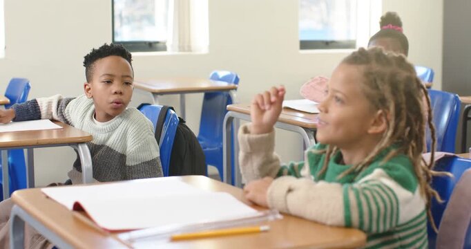 African American boy with dreads responding to peer turning, raising hand at school desk notebook