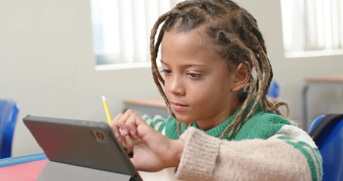 African American boy tapping swiping tablet at school desk with yellow pencil doing work smiling