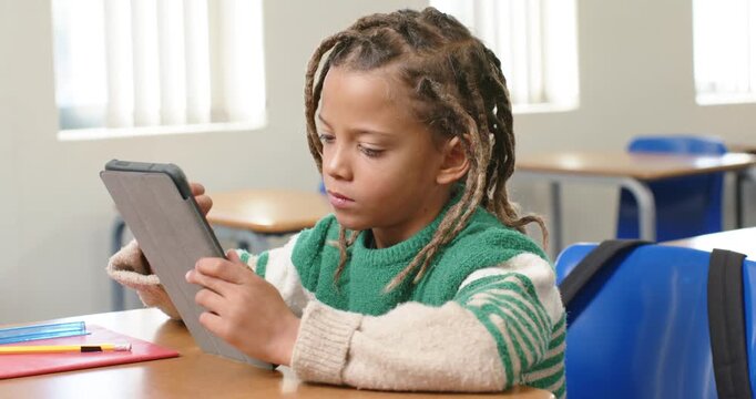 African American child tapping tablet at desk in classroom, lifting tablet to show camera, smiling