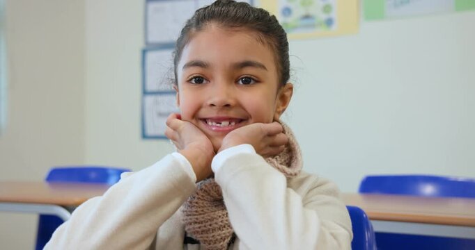 African female child sitting at school desk wearing beige scarf, cupping chin, responding to prompt