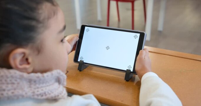 African American teen sitting at classroom desk holding tablet, monitoring target marks for input