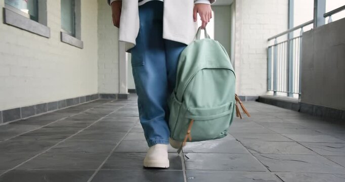 African American teenage female walking toward camera along corridor, carrying mint-green backpack